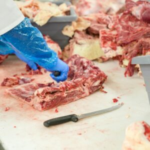 Products Butcher slicing raw meat on a table in NC. Focus on freshness and precision.